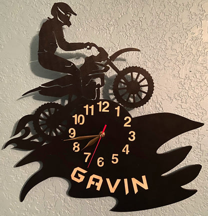 Personalized motocross clock hanging on textured wall with a name cut out.