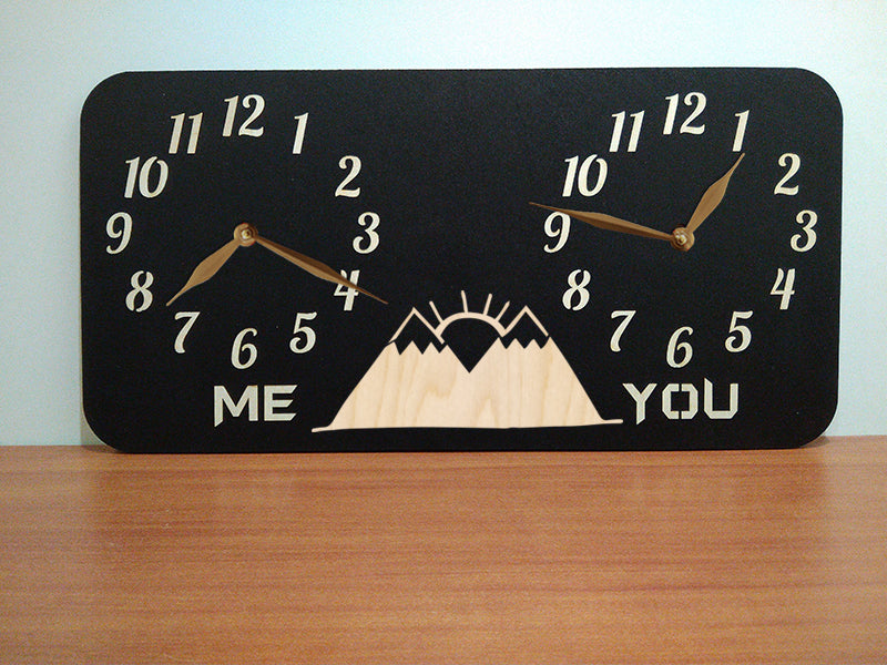 A personalized dual-time wall clock, featuring a moutaine landscape with a sunrise illustration between two sets of hands. The labeles 'ME' and 'YOU' is customized and can be changed to custom inscriptions
